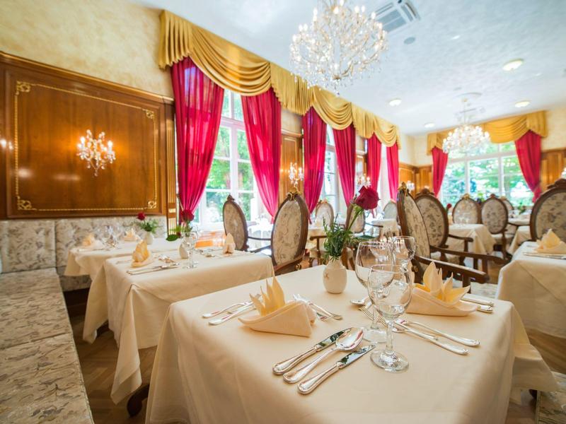Elegant restaurant with set tables, red curtains, and chandeliers.