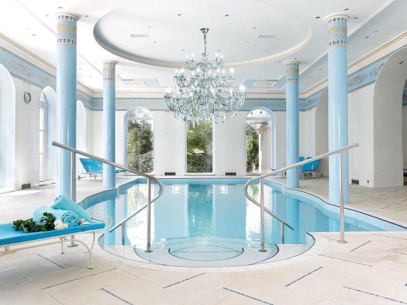 Bright spa with indoor pool, blue-white columns, and a chandelier at the ceiling center.