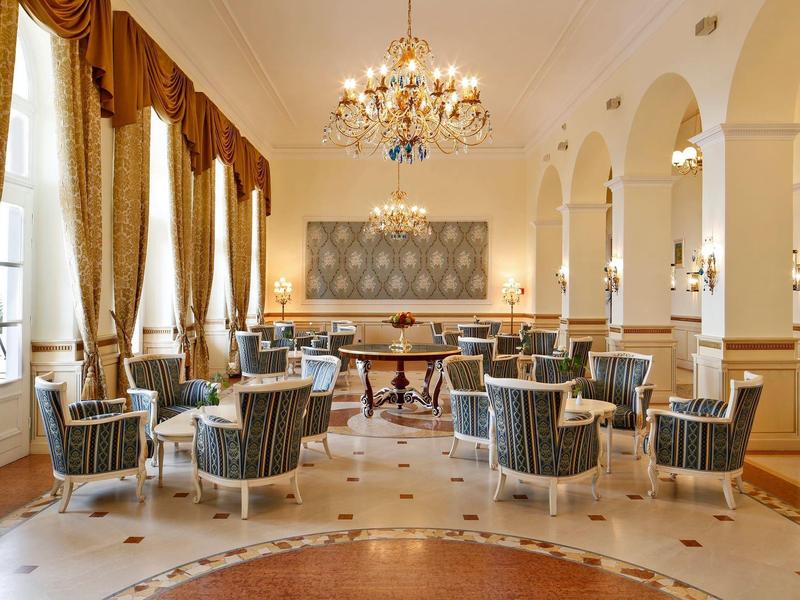 Elegant hotel lounge area with armchairs, tables, and chandeliers in warm lighting.