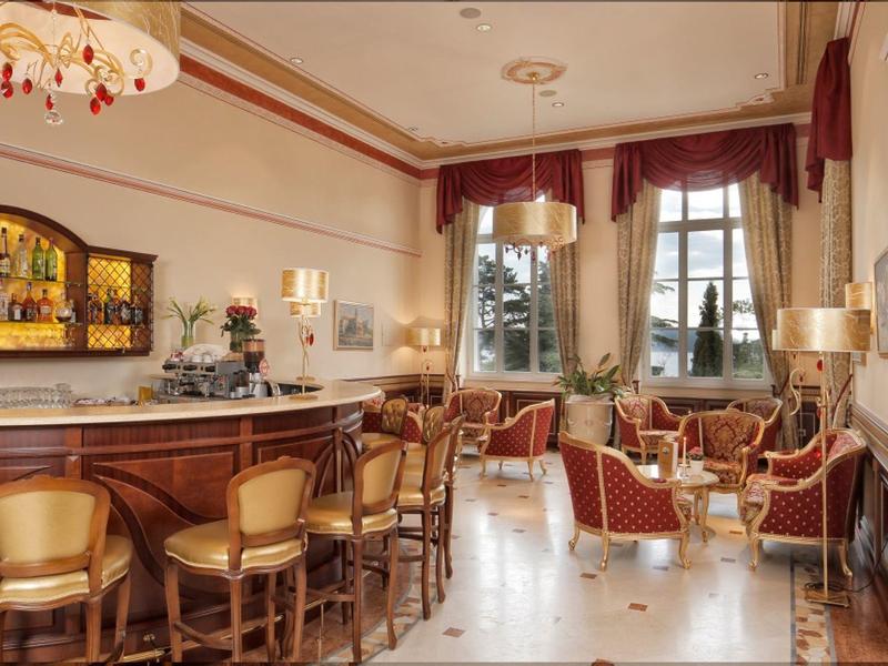 Elegant hotel bar with wooden counter, high stools, and cozy seating area by windows.