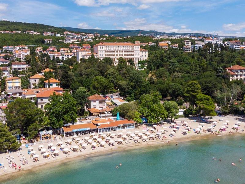 Beach with sunbeds, umbrellas, and a hotel in front of wooded hills