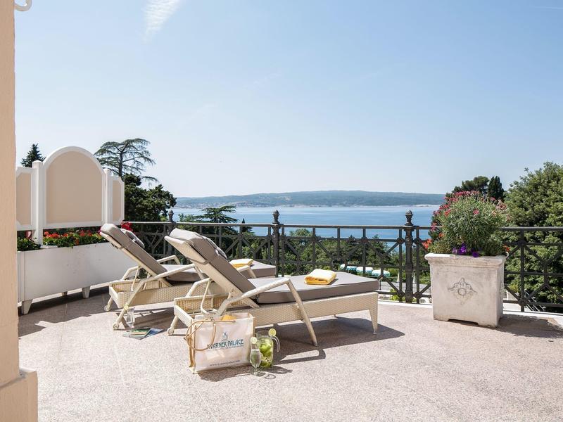 Sunny terrace with lounge chairs and a view of the sea and coastal landscape.