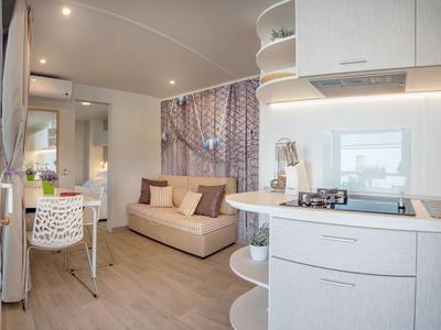 Jasne, nowoczesne mieszkanie z sofą, stołem jadalnym i otwartą kuchnią z płytą grzewczą i półkami.