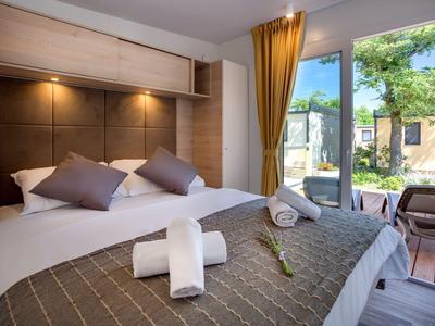 Nowoczesna sypialnia z dużym łóżkiem, poduszkami i dostępem do tarasu z widokiem na ogród