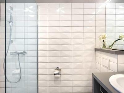 Moderní koupelna s bílými obklady, skleněným sprchovým koutem a umyvadlem.