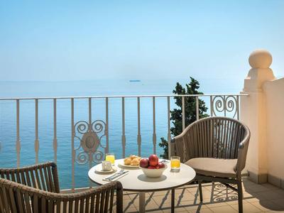 Balkon s stolem a židlemi s výhledem na klidné moře pod jasnou oblohou.