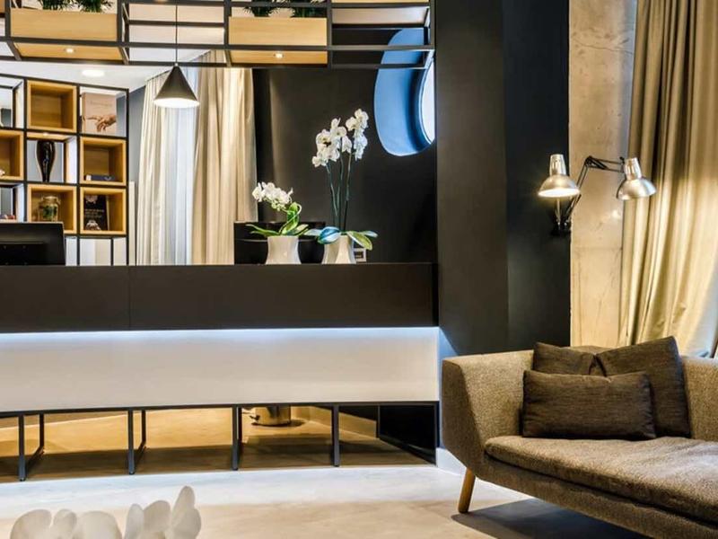 Modern hotel lounge area with reception desk, bookshelf wall, and cozy sofas in warm tones.