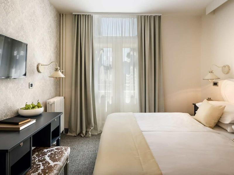 Cozy hotel room with large bed, wall-mounted TV, and light curtains on the window.