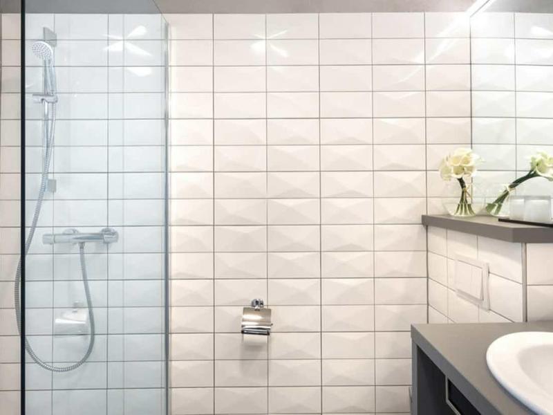 Modern bathroom with white tiled walls, glass shower, and sink with mirror.