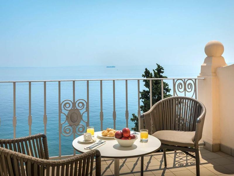 Balcony with table, chairs, and view of calm sea under clear sky.