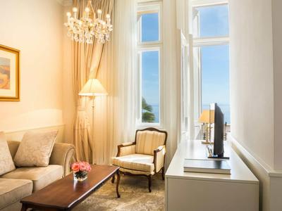 Salon lumineux avec canapé, fauteuil, lampadaire et télévision devant de grandes fenêtres avec vue sur la mer.