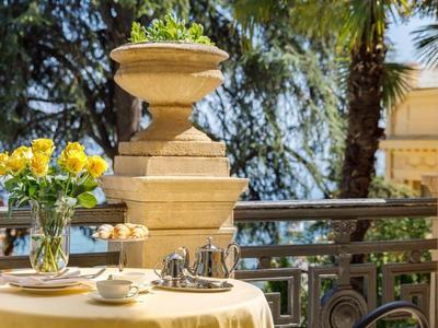 Balcon avec des vases de fleurs et une table avec une théière devant un arrière-plan verdoyant.
