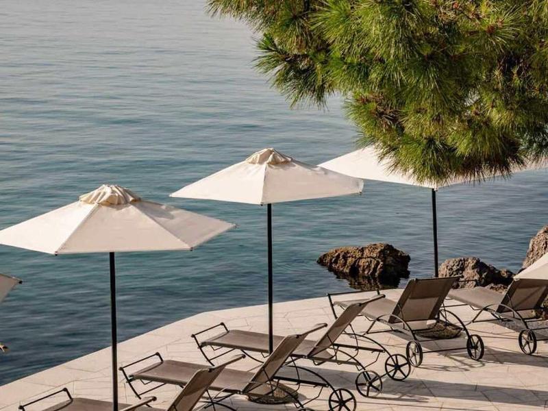 Empty lounge chairs and umbrellas by the calm lakeside under a tree.