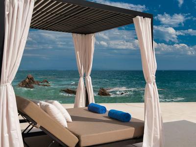 Plaża z wygodną strefą lounge pod pergolą z zasłonami i poduszkami pod niebieskim niebem.