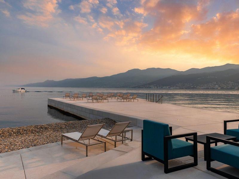 Beach with lounge chairs and seating by the water at sunset with mountains in the background.