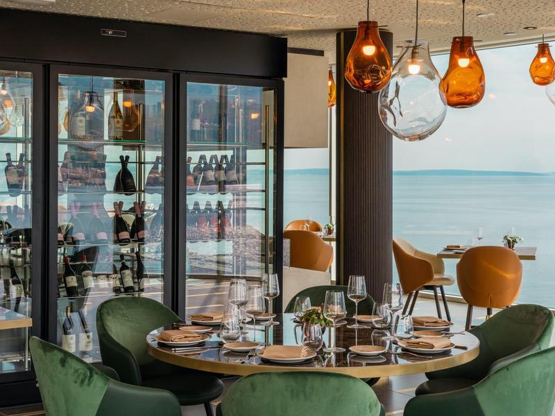 Elegant restaurant with green chairs, round tables, and a sea view.