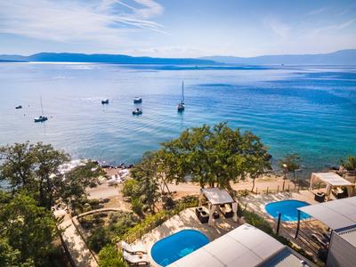 Blick von oben auf einen Hotelpool mit Blick auf das ruhige Meer und Segelboote bei klarem Himmel.