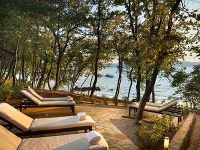 Liegestühle auf einer Terrasse mit Blick auf einen bewaldeten See bei Sonnenuntergang.