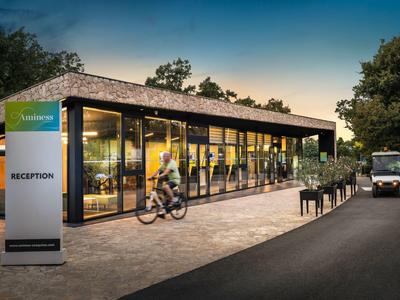 Moderner Empfangsbereich mit Glasfront, Fahrradfahrer und Lieferwagen an der Einfahrt bei Abendlicht.