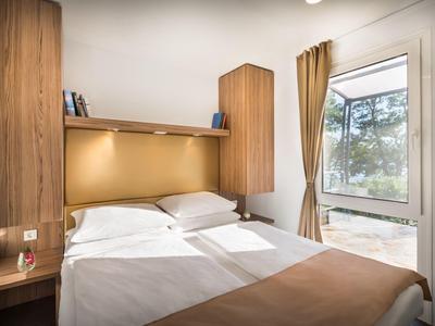 Gemütliches Hotelzimmer mit Doppelbett, Holzverkleidung und großem Fenster mit Blick ins Grüne.