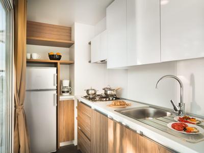 Moderne Küchenecke mit Holzfronten, weißen Schränken, Spüle und Herd in einem hellen Raum