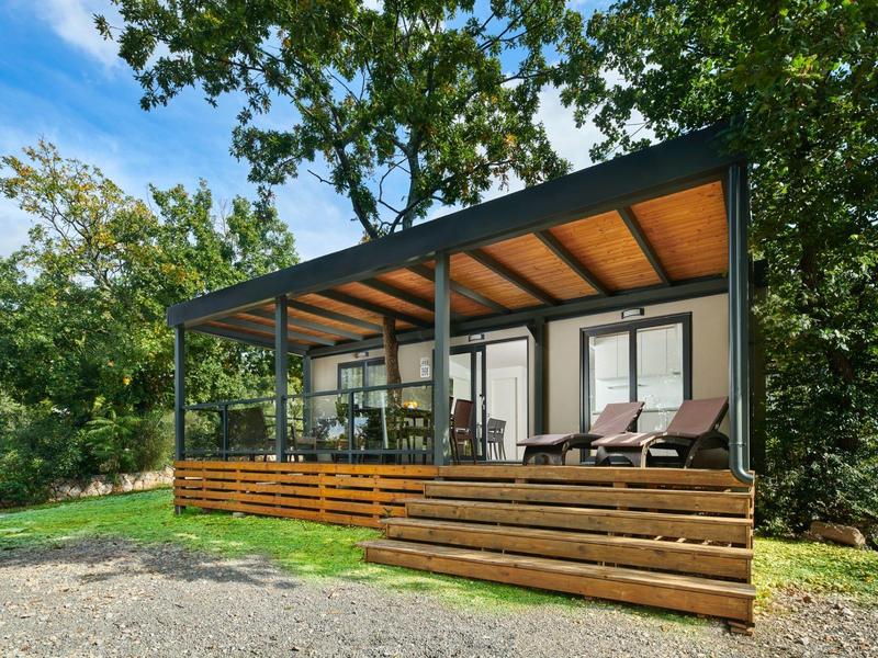 Modernes kleines Haus mit großer Terrasse und Sonnenliegen in grüner Umgebung