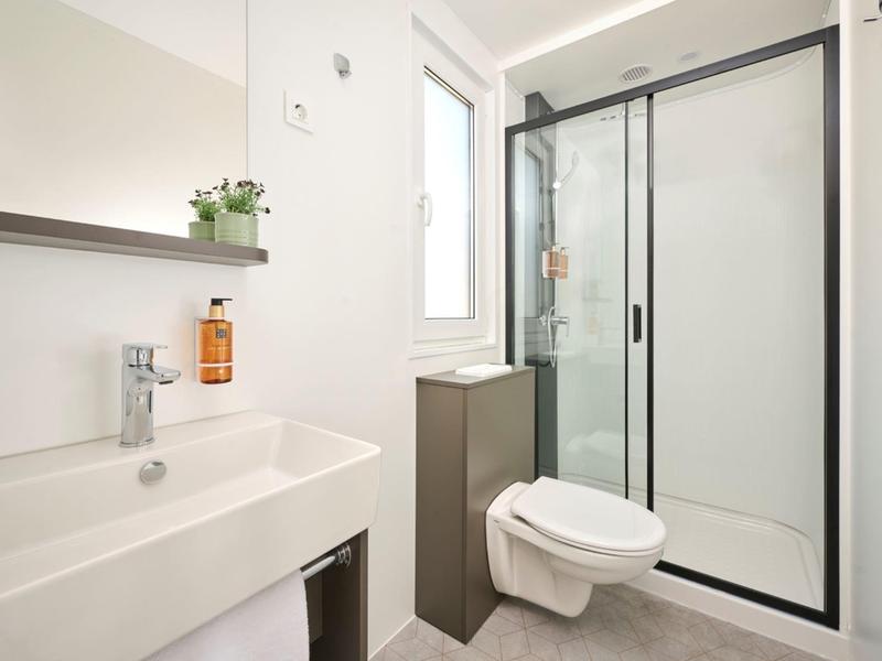 Moderner Hotelbadezimmer mit weißem Waschbecken, Toilette und Duschkabine mit Glasabtrennung.