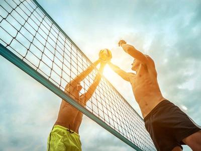 Two men playing beach volleyball at sunset under a cloudy sky.