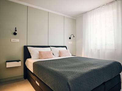 Bright, modern bedroom with large bed, gray blanket, and white curtains.