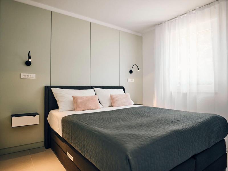 Bright, modern bedroom with large bed, gray blanket, and white curtains.