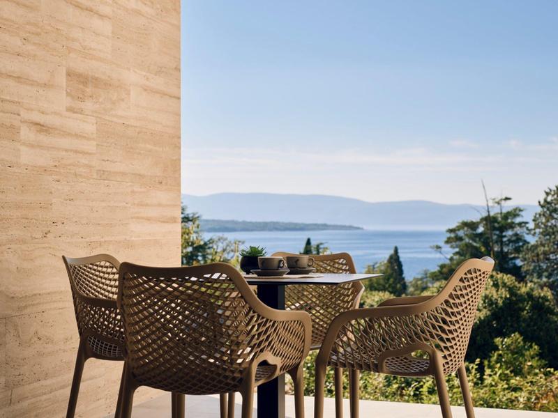 Terrace with two chairs and a table overlooking a garden landscape and the sea.