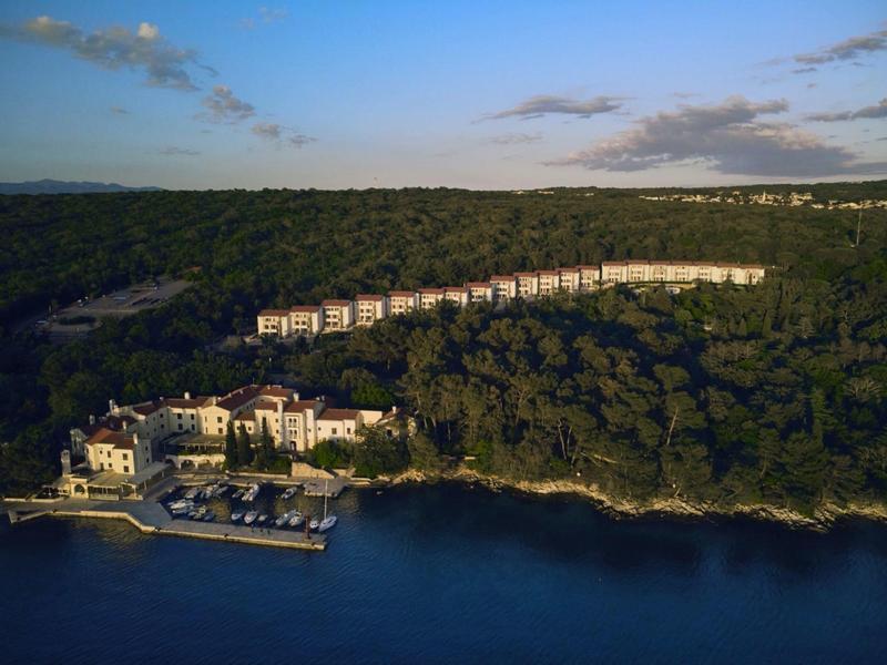Coastal hotel complex with dense forest and several buildings by the water.