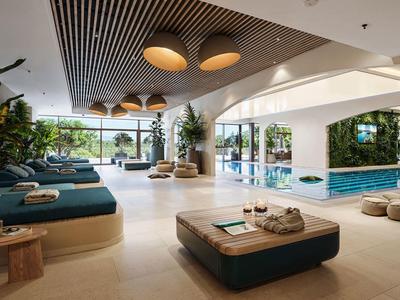 Světlá a moderní krytý bazén s lehátky a výhledem na venkovní bazén.