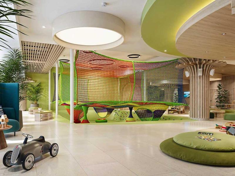 Moderní světlá vnitřní herna s kulatými polštáři a zelenou výzdobou v hotelu.