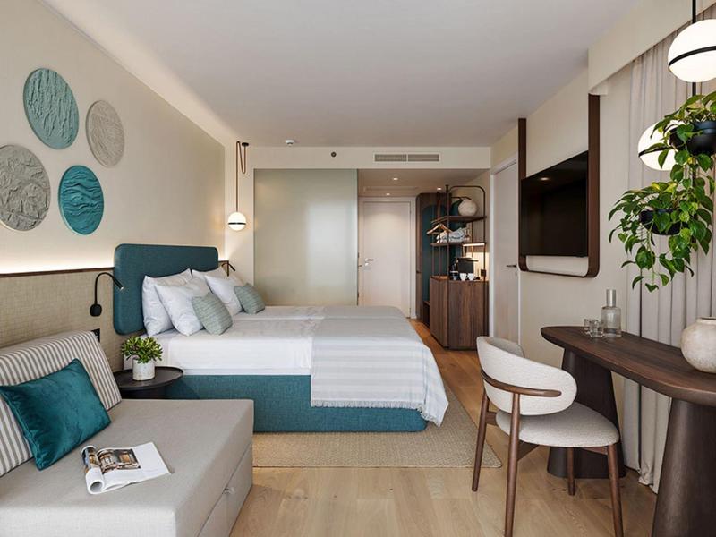 Moderní hotelový pokoj s manželskou postelí, pohovkou, psacím stolem a stylovým zařízením.