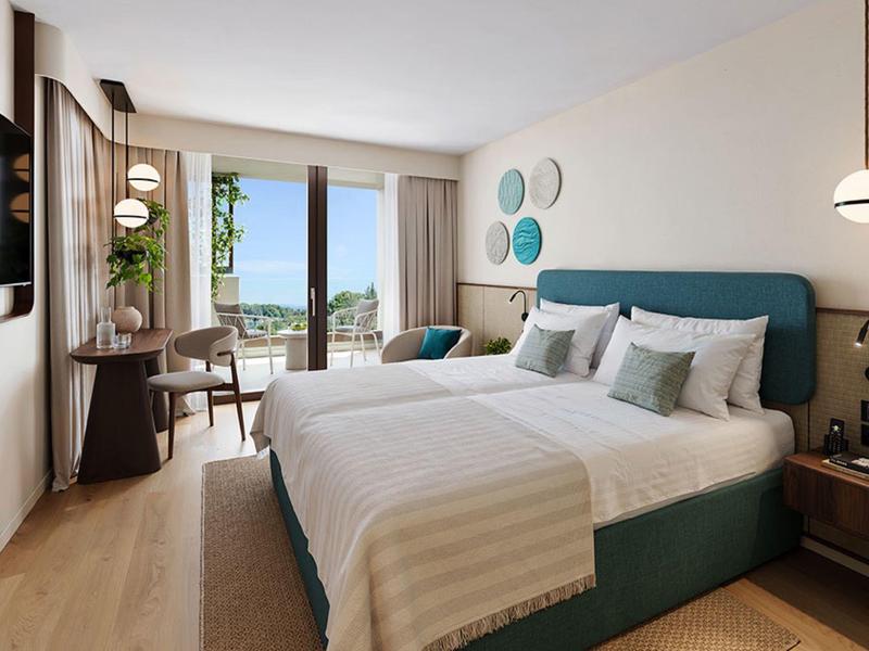 Moderní hotelový pokoj s velkou postelí, balkonem a výhledem na moře.
