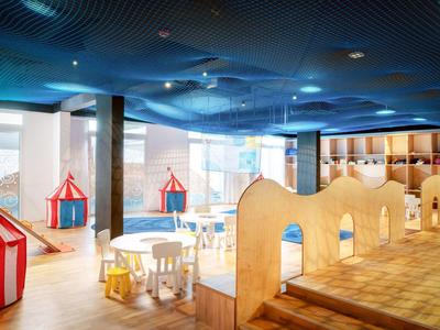 Kinderöffnungsbereich mit buntem Zirkuszelt, Tischen, Stühlen und Holzspielstrukturen.