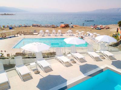 Poolbereich mit Liegestühlen und Sonnenschirmen am Meer mit Bergblick