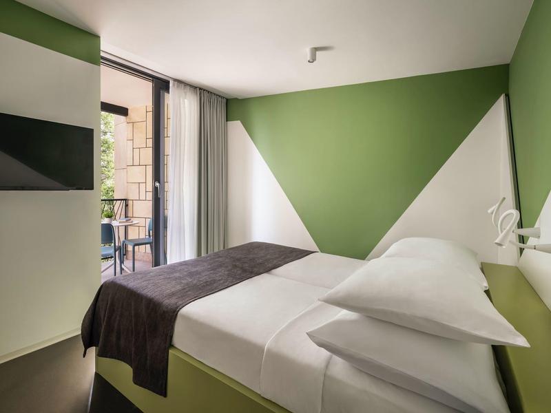 Kleines Zimmer mit grün-weißen Wänden, Doppelbett, Fenster mit Blick auf Balkon.