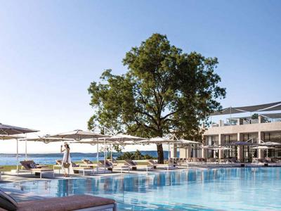 Moderner Hotelpool mit Liegestühlen und Meerblick unter klarem Himmel.