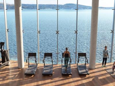 Blick auf ein modernes Spa mit Liegestühlen vor großflächigen Fenstern und einem See im Hintergrund.