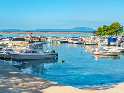 Kleiner Hafen mit Freizeitbooten bei klarem Himmel und ruhigem Wasser in Urlaubsregion.