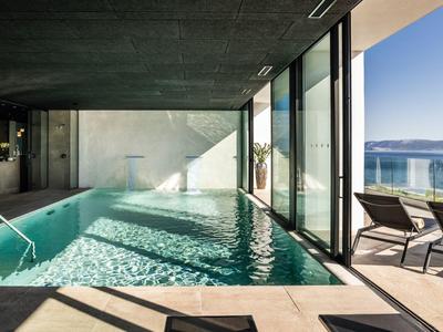 Moderner Indoor-Pool mit großer Glasfront und Blick auf Terrasse und Meer.