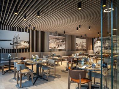 Moderner Hotelrestaurantbereich mit dunklen Wänden, Holztischen und Stühlen, eleganter Beleuchtung.