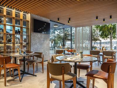 Modernes Hotelrestaurant mit Holzdecke, großen Fenstern und eleganten Tischen und Stühlen.