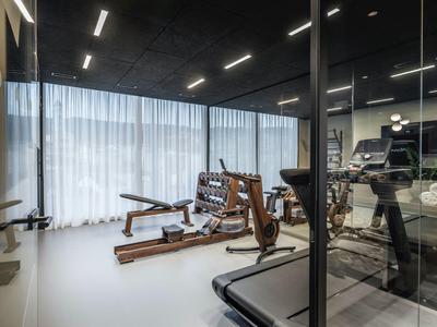 Moderner Fitnessraum im Hotel mit Hanteln, Laufband und Gewichtsbank vor großen Fenstern.