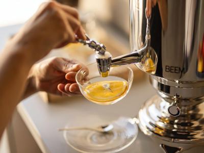 Nahaufnahme einer Hand, die Tee aus einem silbernen Samowar in eine gläserne Tasse gießt.