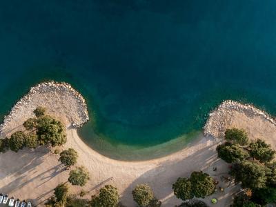 Luftaufnahme einer kleinen Sandbucht mit klarem blauem Wasser und umgeben von Bäumen und Felsen.