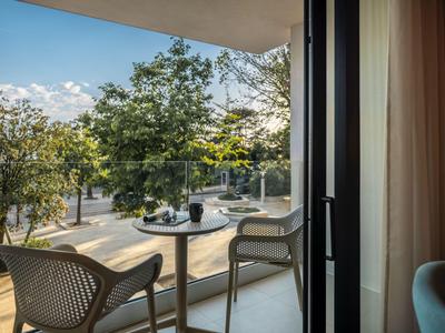 Balkon mit zwei modernen Stühlen und Tisch mit Blick auf einen Baum gesäumten Weg bei schönem Wetter.