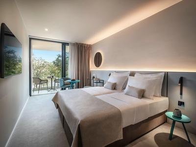 Modernes Hotelzimmer mit Doppelbett, großem Fenster und Blick auf Balkon mit Stühlen.